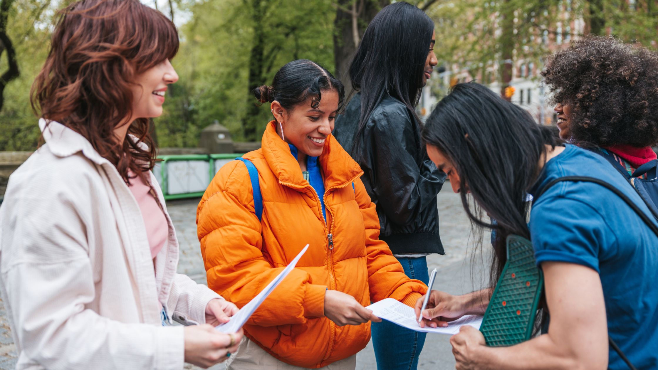Group of people signing registration forms and talking at an outdoor community event in a park.