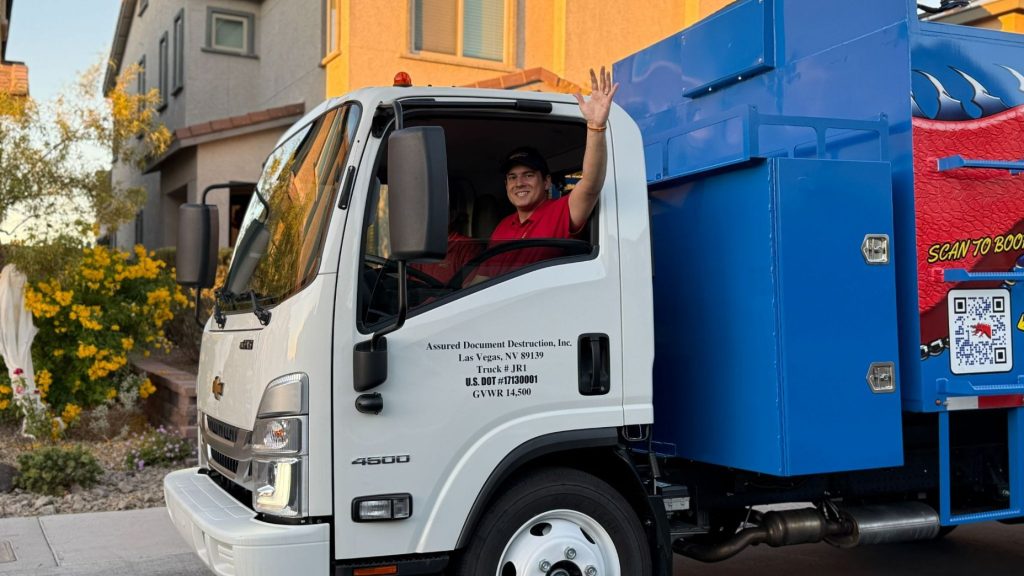 Driver waving from an Assured Document Destruction mobile shredding truck outside a residential home before on-site document shredding.